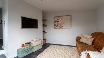 A living room with a brown sofa, a patterned rug, a television mounted on the wall, and a piece of abstract art.