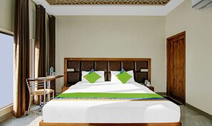A hotel room with a large bed, a wooden headboard, a small table with a chair, a wardrobe, and a window with curtains. - Hotel Royal Salute (Dera Bassi)