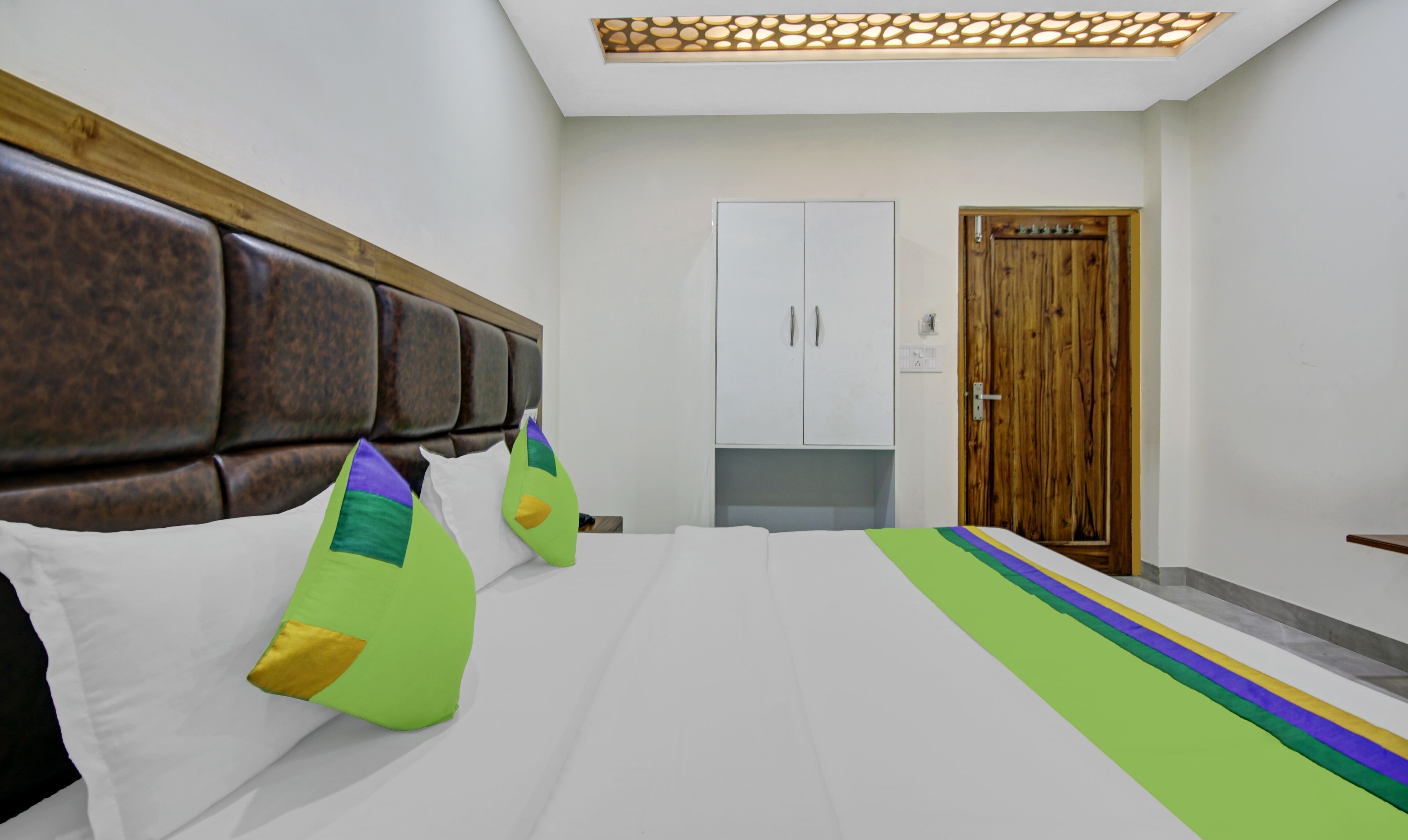 A hotel room with a large bed, a wooden headboard, a wardrobe, and a door.