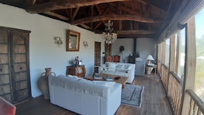 A rustic interior with a wooden ceiling, white sofas, a wooden table, and a chandelier.