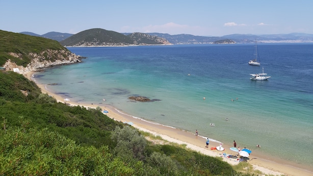 A coastal beach with clear turquoise waters, a sandy shore, and a few boats.