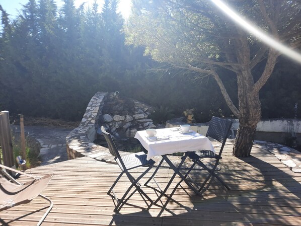 A wooden deck with a table and chairs, surrounded by stone walls and trees.