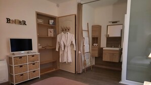 Een slaapkamer met een televisie, opbergmogelijkheden, een kledingkast en een zichtbare badkamer door een geopende deur.