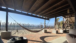 A beachside patio with a hammock, outdoor seating, and a view of the ocean.