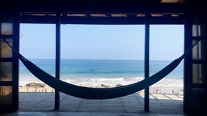 A hammock suspended between wooden beams, overlooking a beach with waves and a clear sky.
