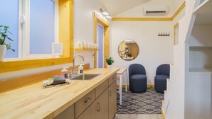 Una cocina compacta con encimera de madera, un lavamanos y un espejo. Hay dos sillas y una mesita.
