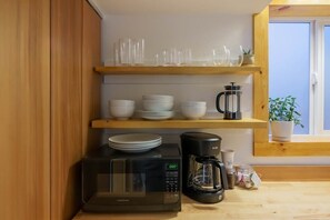 A kitchen with a microwave, coffee maker, and shelves with dishes and glasses.