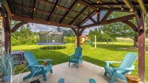 An outdoor patio with Adirondack chairs, a trampoline, and a play structure in the background. - Suite 112: Comfort at Rock Spring Resort (Rock Spring)