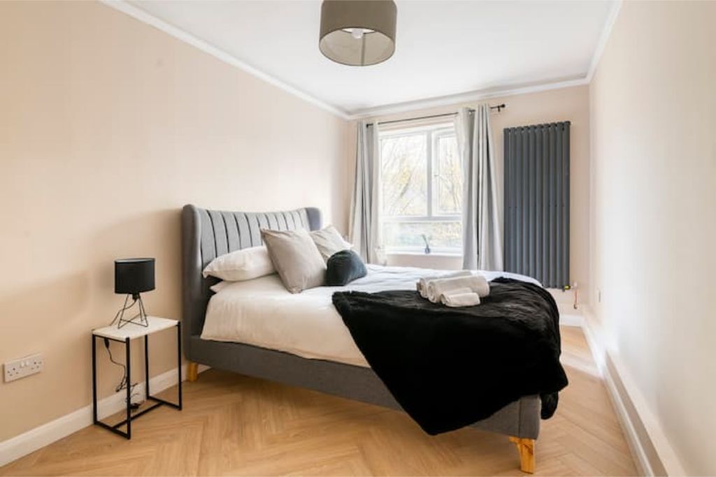 Un dormitorio moderno con cama, lámpara de noche y ventana con cortinas.