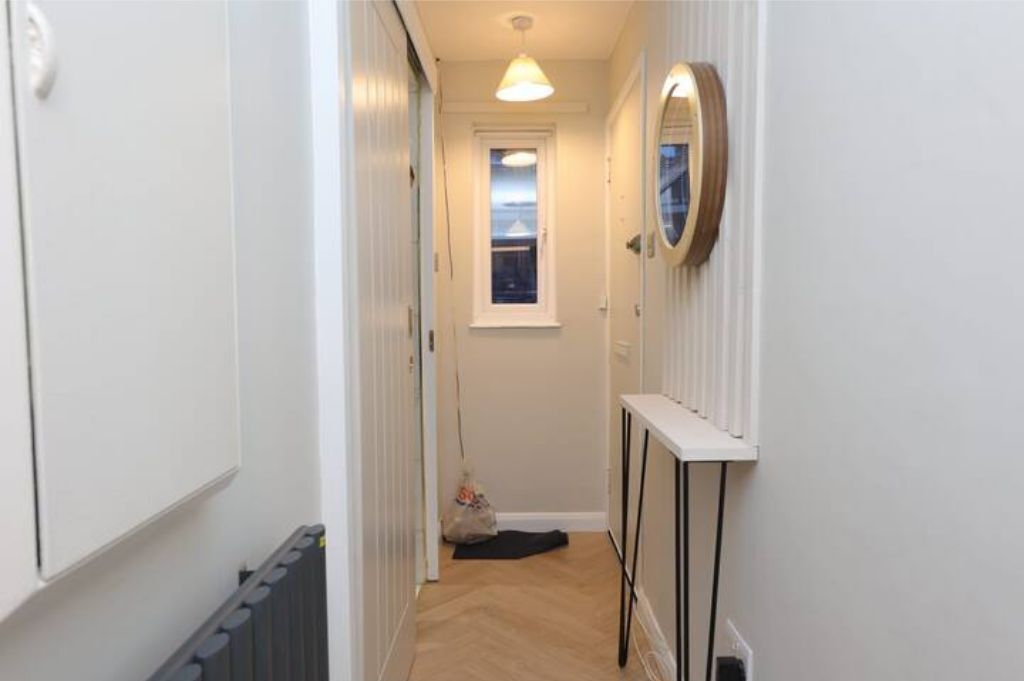 A narrow hallway with a radiator, a window, and a mirror on the wall.