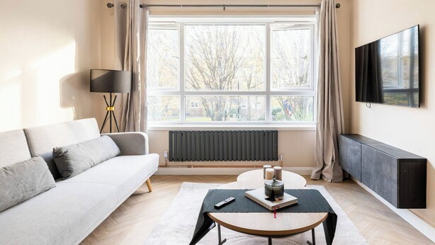 Un salon moderne comprenant un canapé, une table basse, un lampadaire, un radiateur et un téléviseur fixé au mur.