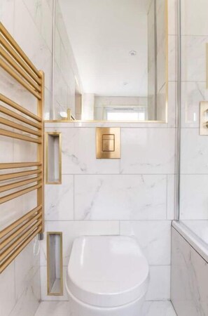 A modern bathroom with a white toilet, a wooden towel rack, and a gold-framed mirror.