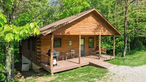 A small wooden cabin with a porch, a grill, and a table and chairs.