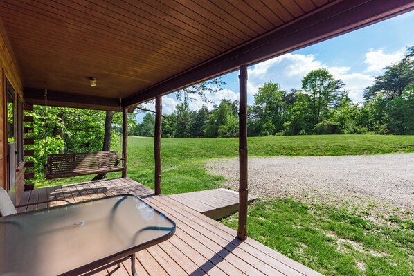 A covered outdoor area with a table and bench, overlooking a grassy field and trees.