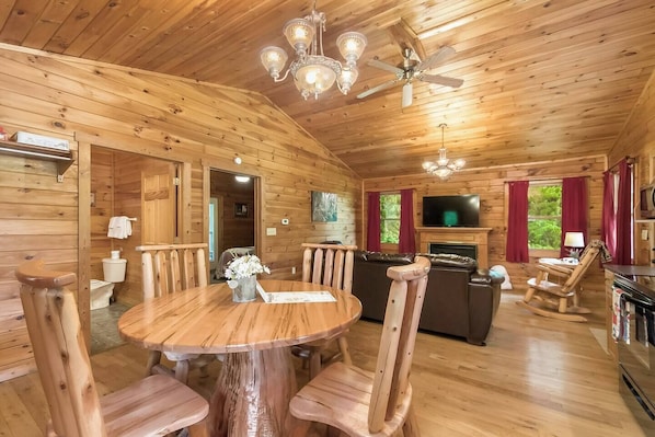 A wooden cabin interior with a dining table, chairs, a sofa, a television, and a fireplace.