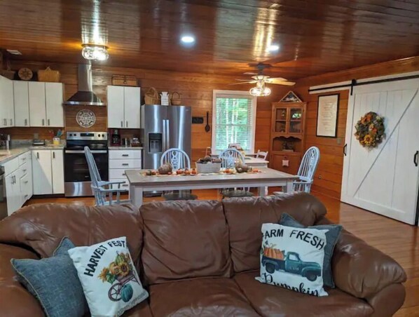 L’intérieur d’une cabane comprend un coin repas, une cuisine et un canapé en cuir marron agrémenté de coussins décoratifs.