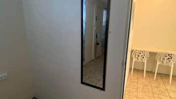 Ein Zimmer mit gefliestem Boden, einer Tür mit Spiegel und zwei weißen Stühlen im Hintergrund.