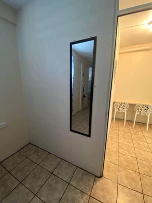 A room with a tiled floor, a door with a mirror, and two white chairs in the background. - Cayo Enrique at Guayacán Guest House (Lajas)