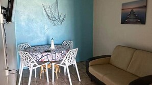 A dining area with a table and chairs, a ceiling fan, a wall-mounted TV, and a sofa. - Cayo Enrique at Guayacán Guest House (Lajas)