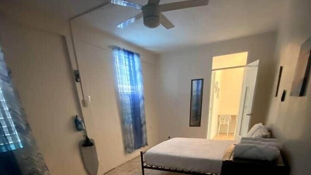 A bedroom with two beds, a ceiling fan, a window with curtains, and a door leading to another room. - Cayo Enrique at Guayacán Guest House (Lajas)