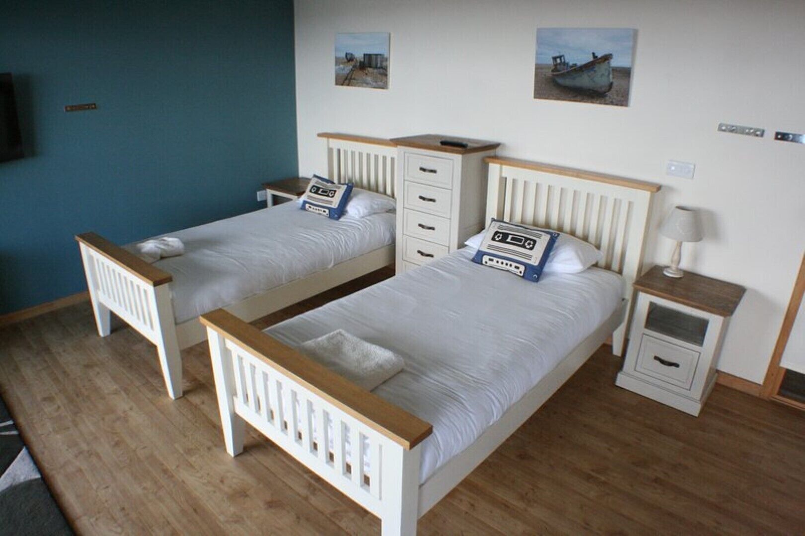 A room with two single beds, each with a wooden headboard and a bedside table with a lamp.