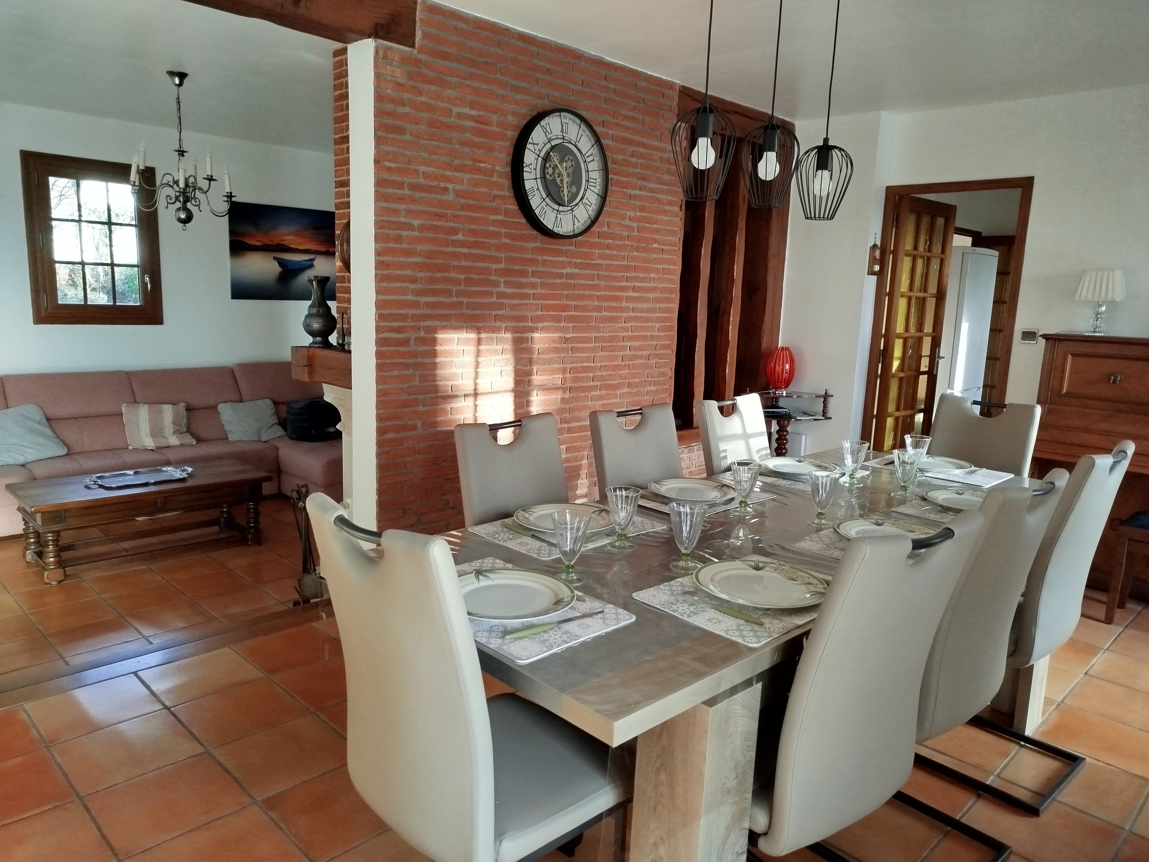 A dining area with a brick wall, a large clock, and a chandelier.