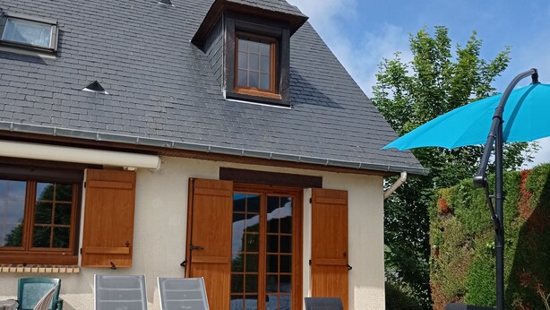 Une maison avec un patio carrelé, une grande fenêtre et une porte avec des volets.