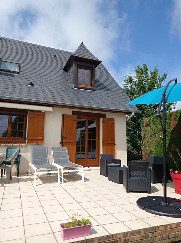 Een huis met een betegeld terras, een groot raam en een deur met luiken.