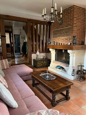 Een woonkamer met een open haard van baksteen, een houten salontafel en een roze bank.
