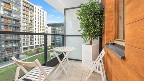 Un balcone con vista su un moderno edificio condominiale, una pianta in vaso e un piccolo tavolo con sedie.