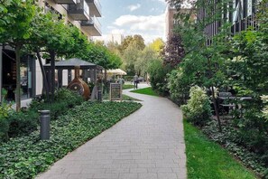 A pathway flanked by greenery and modern buildings, leading to a gazebo.