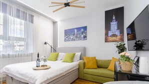 A modern bedroom with a bed, a green sofa, and a cityscape painting. - Comfortable studio on Twarda in Center (Warszawa)
