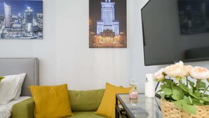 A living room with a green sofa, mustard pillows, a glass coffee table with a vase of flowers, and a framed cityscape picture on the wall. - Comfortable studio on Twarda in Center (Warszawa)
