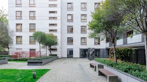 Un patio con un sendero empedrado, bancos y un edificio con múltiples ventanas.