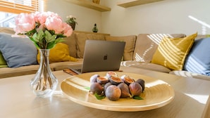 Una computadora portátil sobre una mesa de madera con un plato de higos y un jarrón de flores.