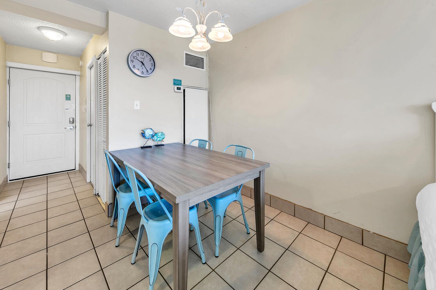 A dining area with a wooden table and blue chairs, a clock, and a ceiling light fixture.