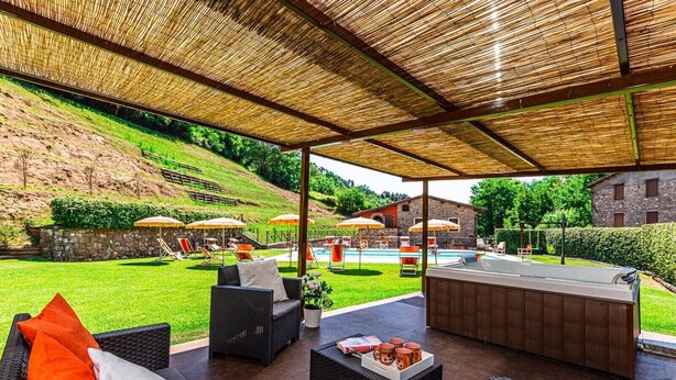 An outdoor patio area with wicker furniture, a hot tub, and umbrellas. - A spacius and comfortable apartment with a large terrace (Toscana)