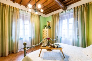 Een slaapkamer met een houten bed, een nachtkastje met dienblad, een radiator en een raam met gordijnen.