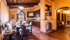 A kitchen with a stone fireplace, wooden ceiling beams, and a dining area with a bench and chairs. - A spacius and comfortable apartment with a large terrace (Toscana)