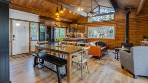 Une cuisine spacieuse dotée d’appareils électroménagers modernes, un coin repas avec un banc et un coin salon confortable avec une cheminée.