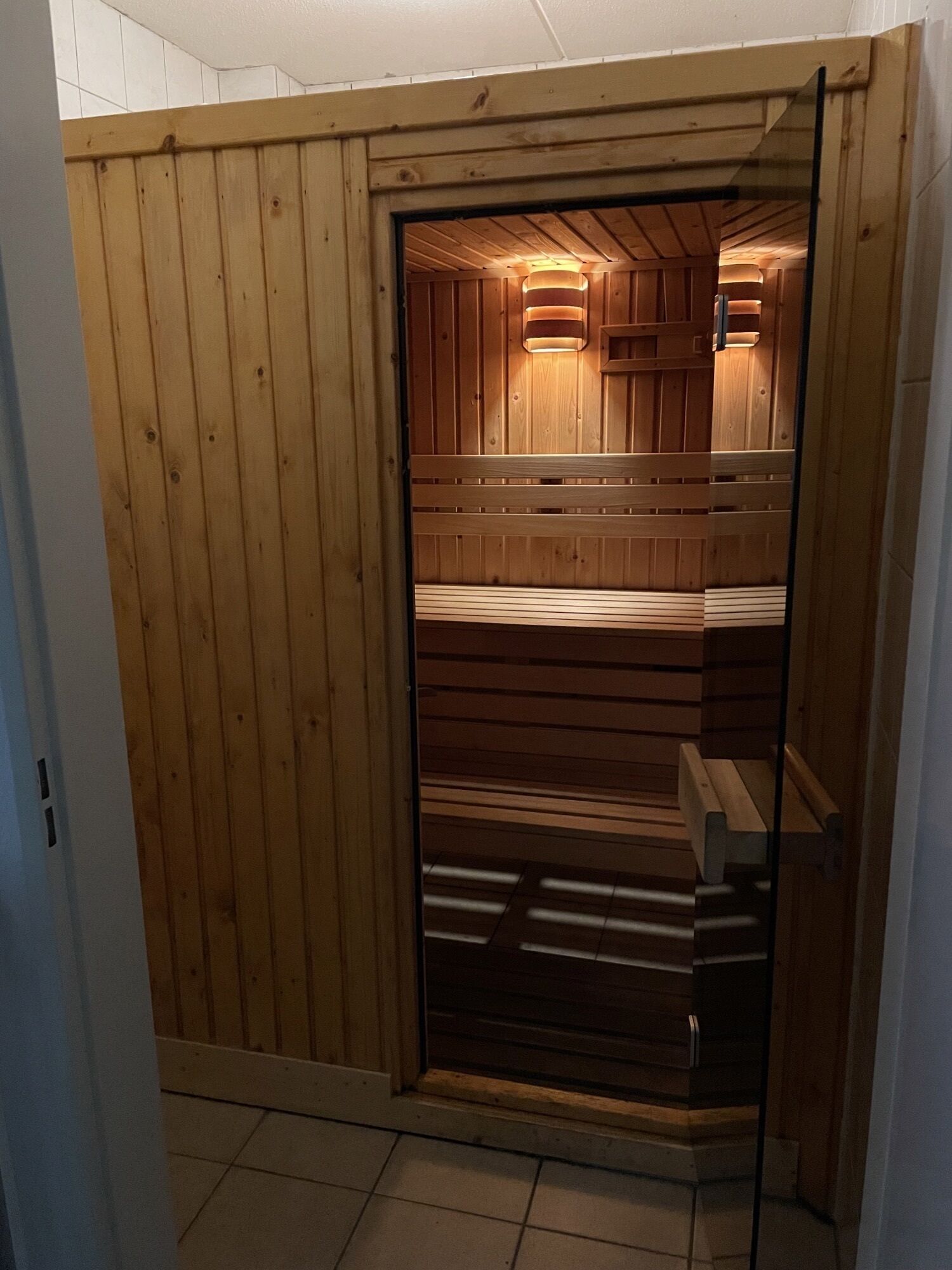 Una sauna amb parets i bancs de fusta, un terra de rajola i una porta.