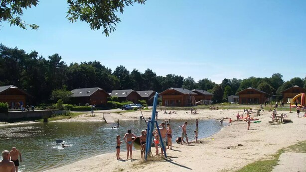 Un complexe hôtelier au bord d’un lac, avec des chalets en bois, une plage de sable et une zone aménagée pour la baignade.