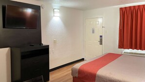 Une chambre d’hôtel avec un lit, un bureau, un téléviseur fixé au mur, une porte et une fenêtre avec des rideaux.