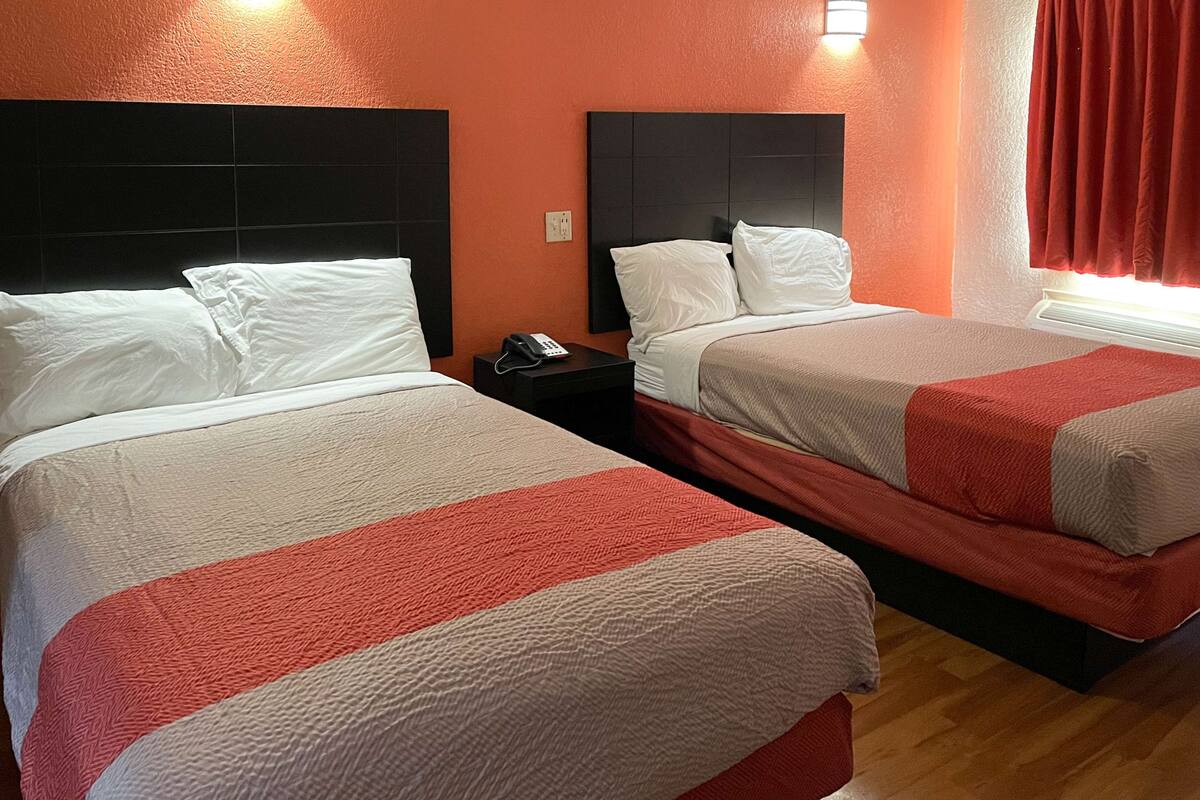 Two beds with white and red bedding, a phone on the nightstand, and a red curtain on the window.