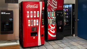 Trois distributeurs de boissons, dont un distributeur de glaçons et deux machines de la marque Coca-Cola, sont installés dans un espace commercial.