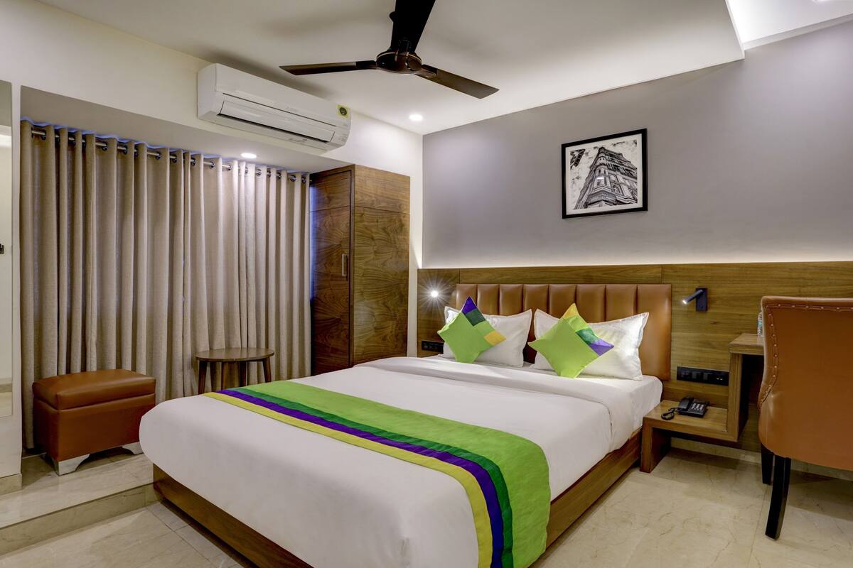 Habitación de hotel con cama, una silla, mesita de noche, aire acondicionado y ventilador de techo.