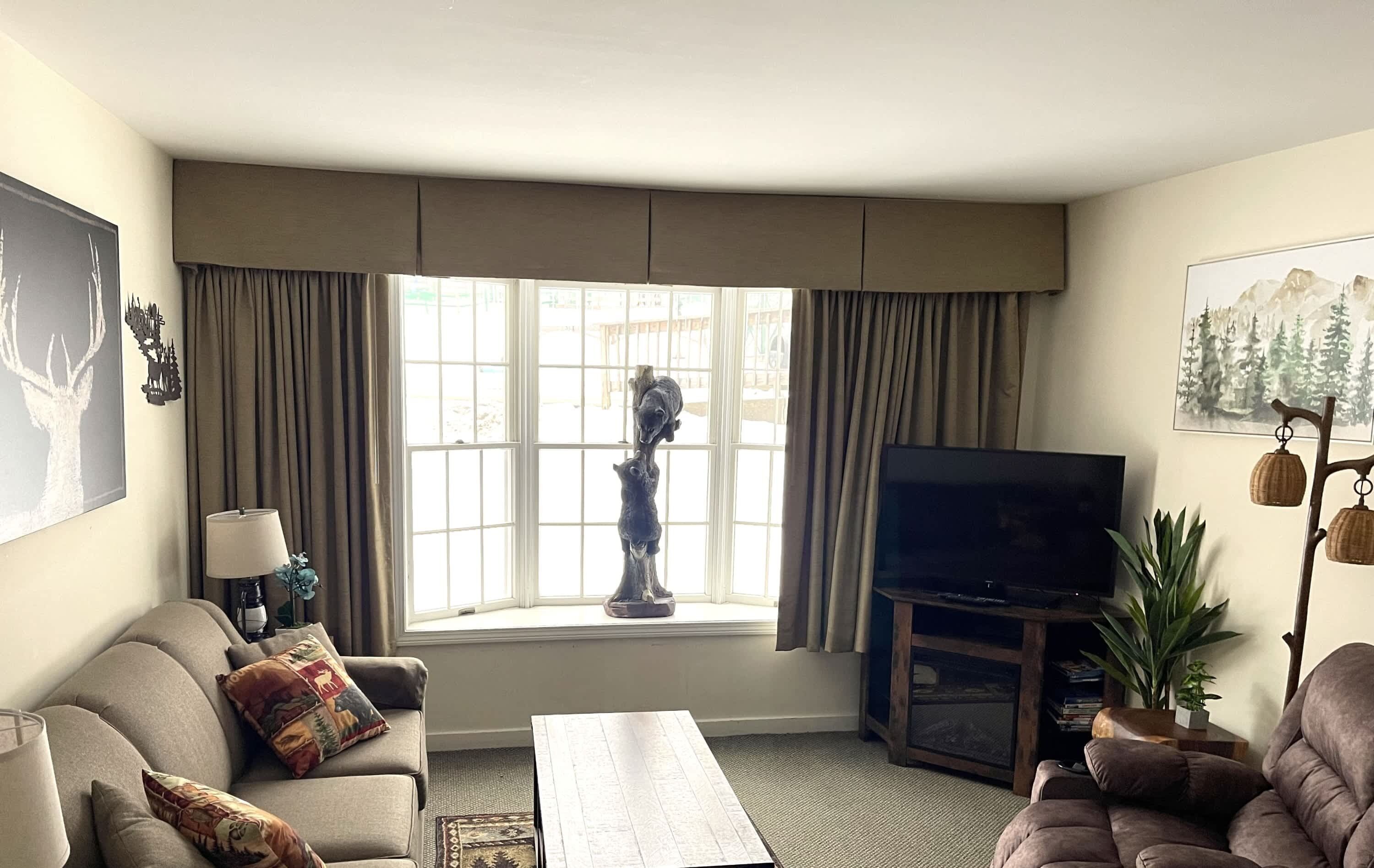 A living room with a sofa, a coffee table, a TV stand, and a window with curtains.