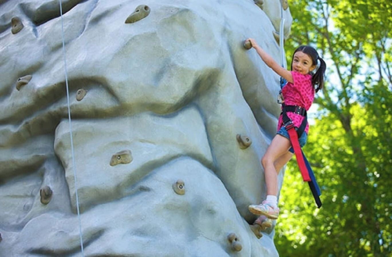 Eine Person erklimmt eine hohe Kletterwand mit Griffen.