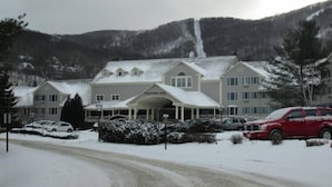 Un edificio ampio con un ingresso coperto e numerose finestre, immerso in un paesaggio innevato con auto parcheggiate.