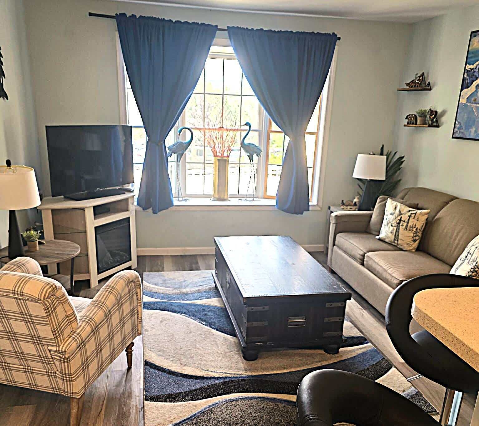 A living room with a television, sofa, coffee table, and a decorative window with curtains.
